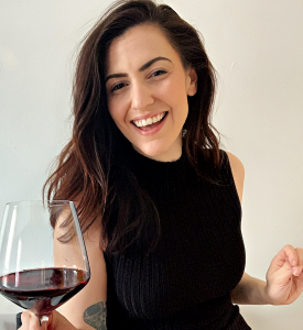 Renee wearing a black top smiling with a glass of red wine