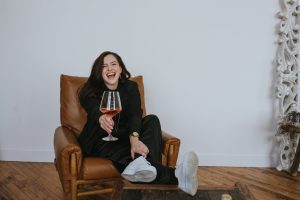 Renee siting in a leather chair with glass of red wine laughing