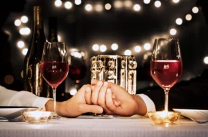 Two people holding hands at a table each with a glass of red wine.